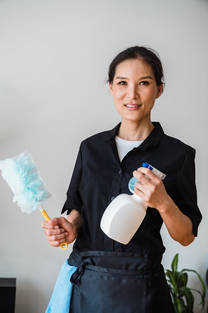 hero-img A female housekeeper smiling while holding cleaning tools indoor.